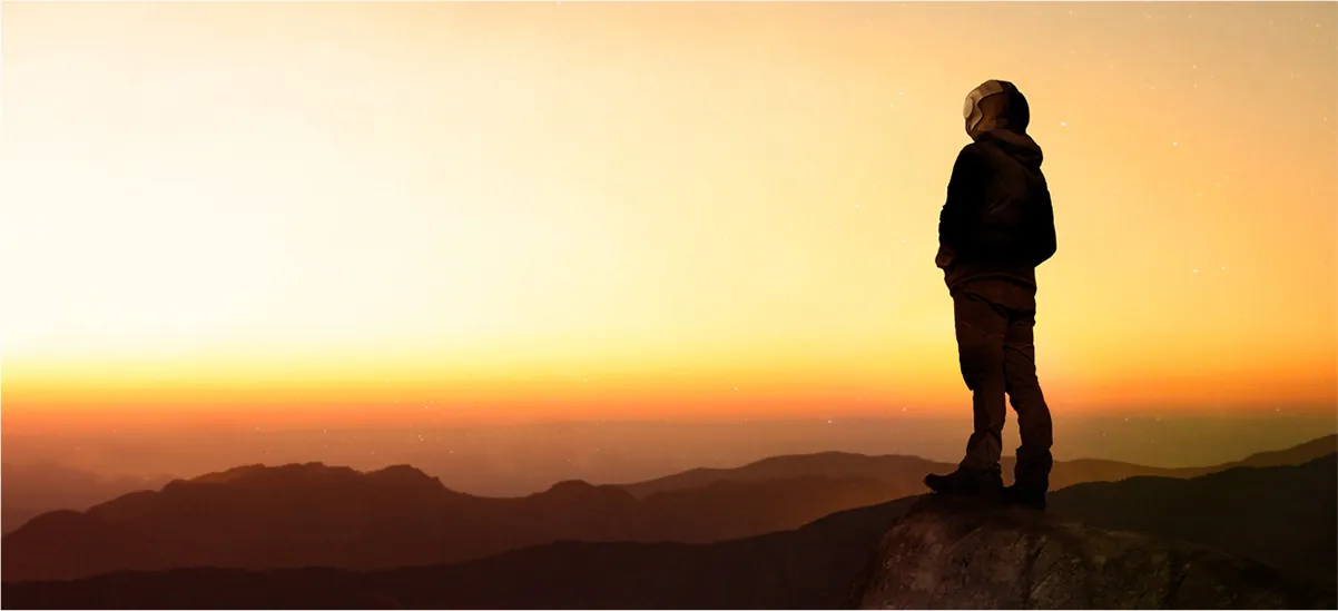 Person standing on a hilltop at sunset, silhouetted against a dramatic sky